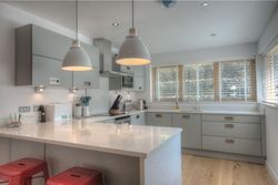 Modern kitchen with grey cabinets, pendant lights, and large windows with wooden blinds
