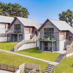 Modern holiday homes with wooden and stone exteriors, large glass balconies, and well-kept lawns.