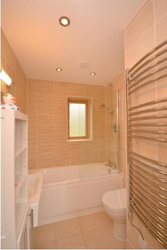 Modern bathroom with bathtub, heated towel rail, shelving, and small window.