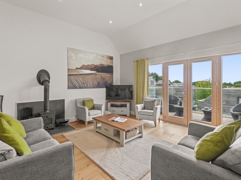 Modern living room with grey sofas, wood stove, TV, and large windows to a balcony.