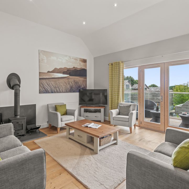 Modern living room with grey sofas, wood stove, TV, and large windows to a balcony.