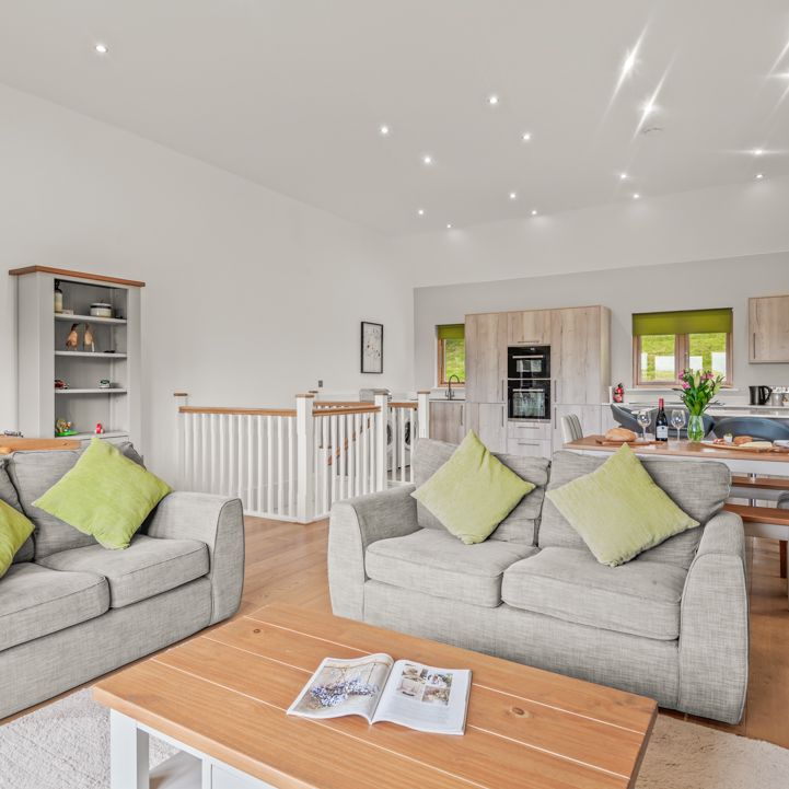 Modern open-plan living room and kitchen with neutral decor, green accents, and comfortable seating.