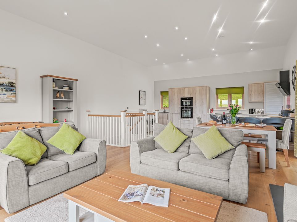 Modern open-plan living room and kitchen with neutral decor, green accents, and comfortable seating.