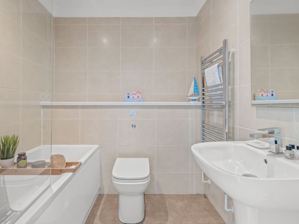 Modern bathroom with beige tiles, bathtub, toilet, sink, and towel rail