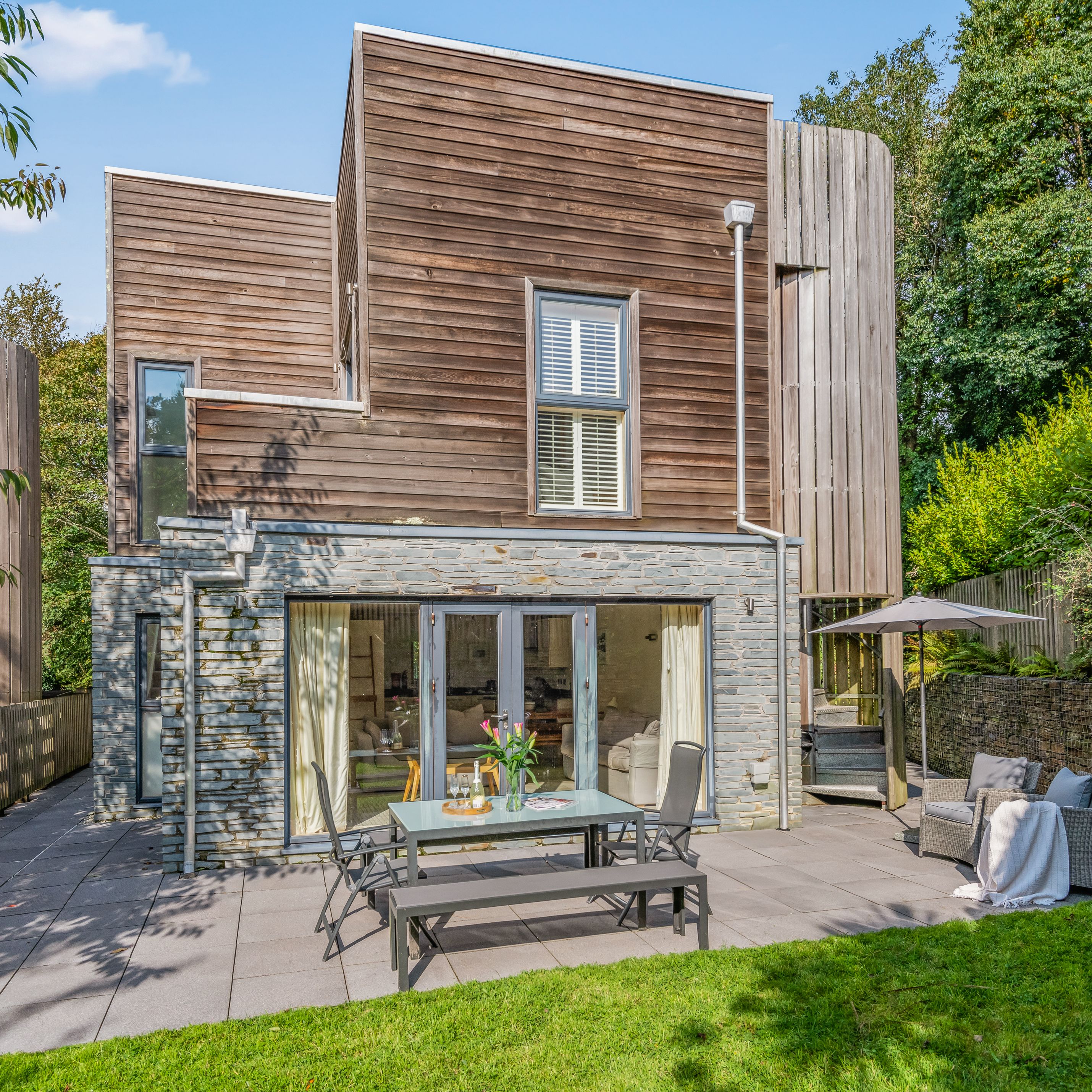 Modern house with wooden and stone exterior, patio, and garden
