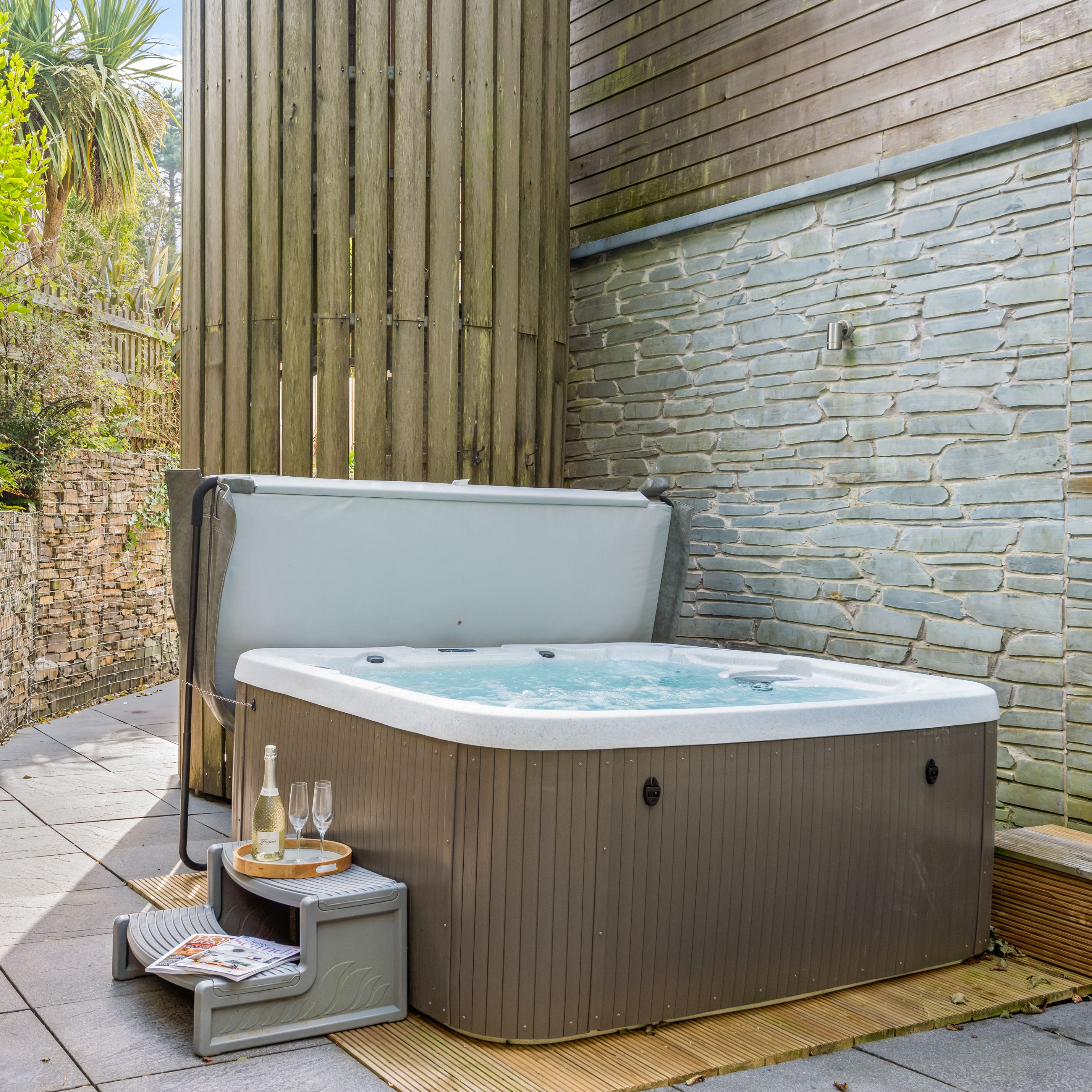 Outdoor hot tub with steps, drinks, and greenery