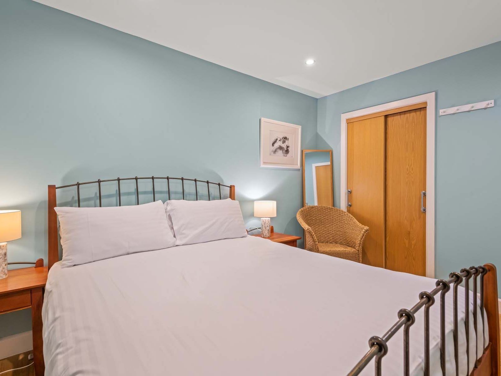 Cozy bedroom with a double bed, wicker chair, wooden nightstands, lamps, and teal walls.