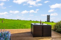 Outdoor patio with table and chairs overlooking a grassy field and a modern tower structure in the distance.
