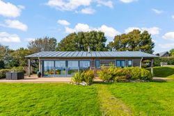 Modern single-story house with large windows, surrounded by green lawn and trees