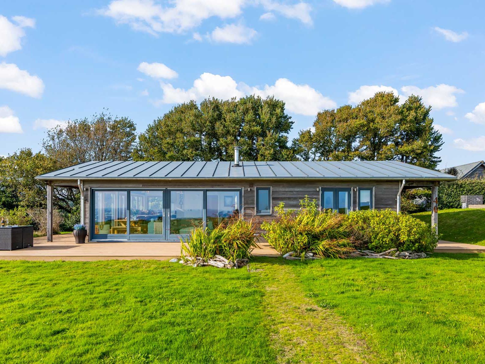Modern single-story house with large windows, surrounded by green lawn and trees