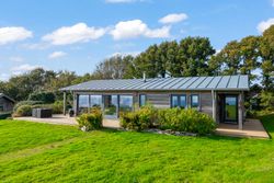 Modern wooden cabin with large windows and deck surrounded by grass and trees