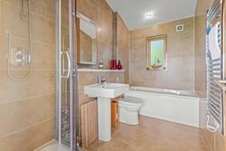 Modern bathroom with beige tiles, shower, sink, toilet, and bathtub.