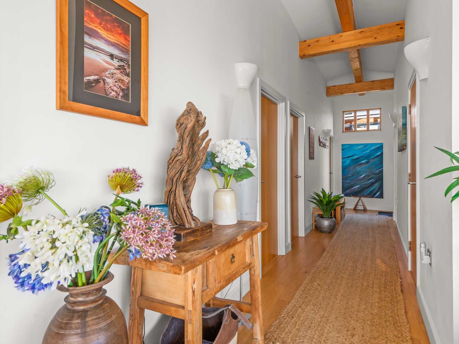 Bright and decorated hallway with wooden beams, artwork, flowers, and rustic furniture.