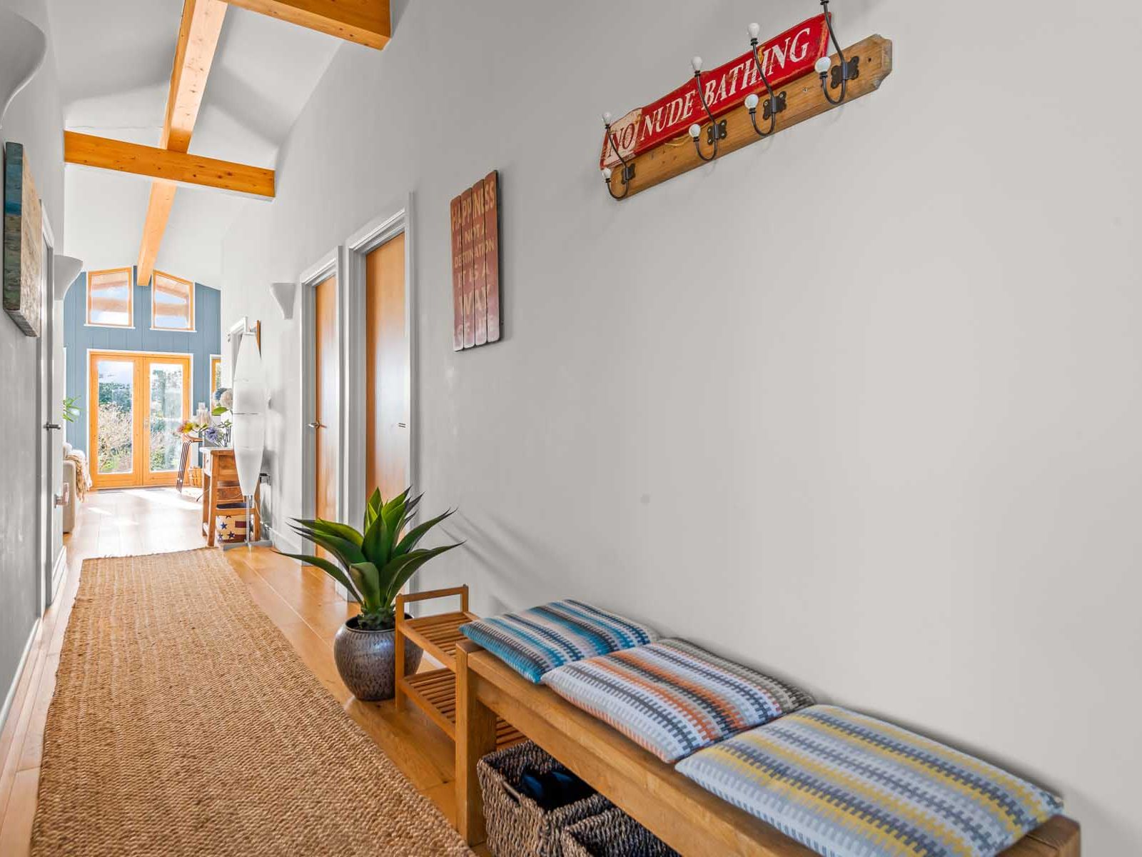 Bright hallway with wooden ceiling beams, cushioned bench, and a 'No Nude Bathing' sign on the wall.