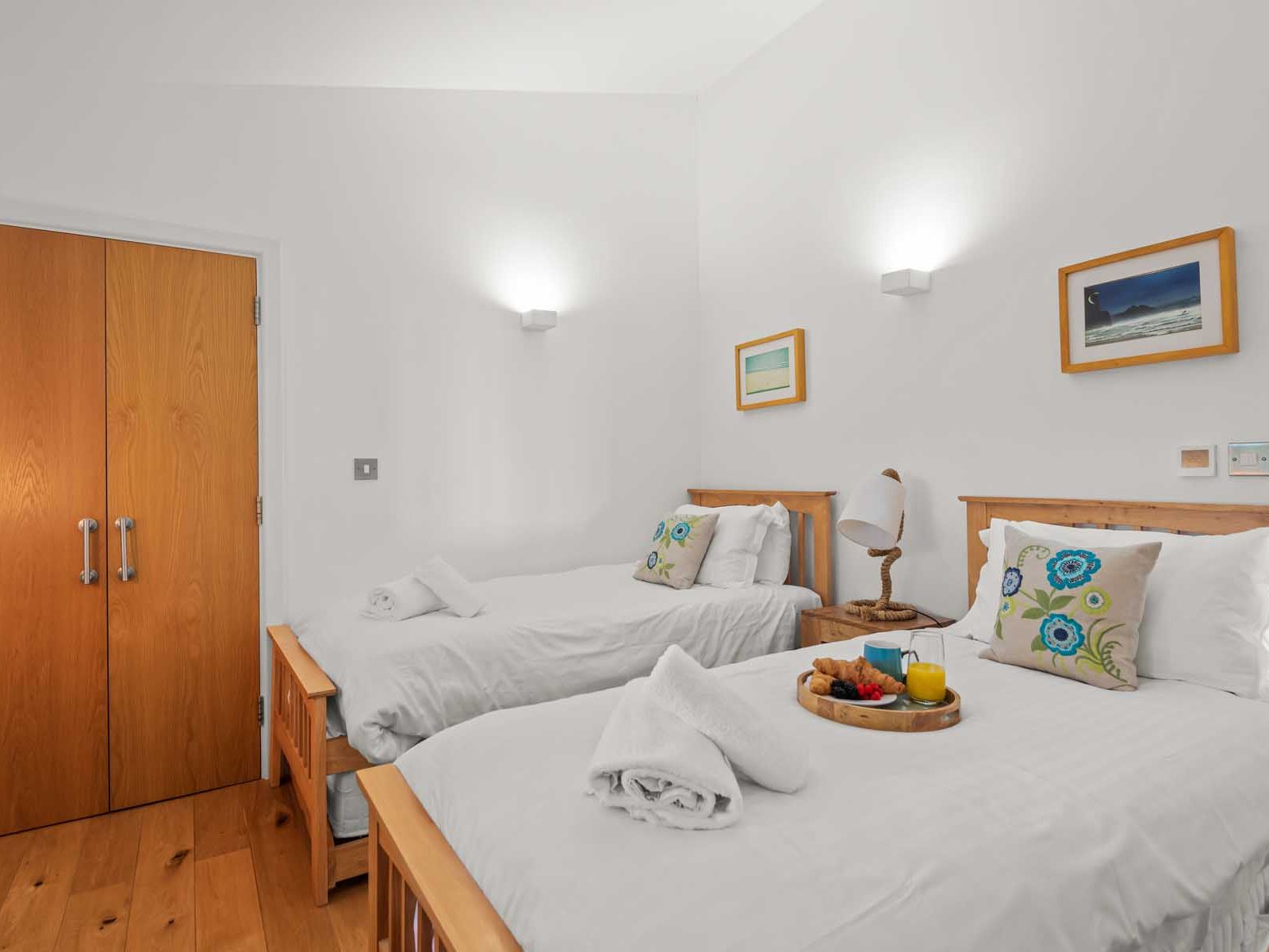 Bright twin bedroom with wooden beds, white linens, decorative pillows, and a breakfast tray.
