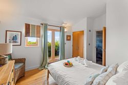 Bright bedroom with large window, wicker chair, and breakfast tray on white bed linens