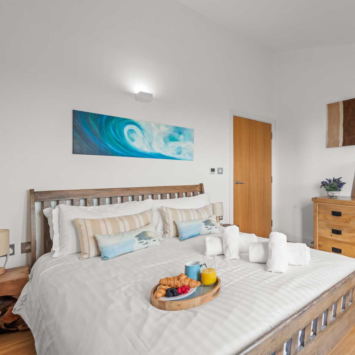 Cozy modern bedroom with a wooden bed, wicker chair, dresser, and breakfast tray on the bed