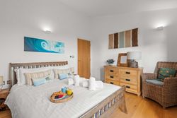 Cozy modern bedroom with a wooden bed, wicker chair, dresser, and breakfast tray on the bed
