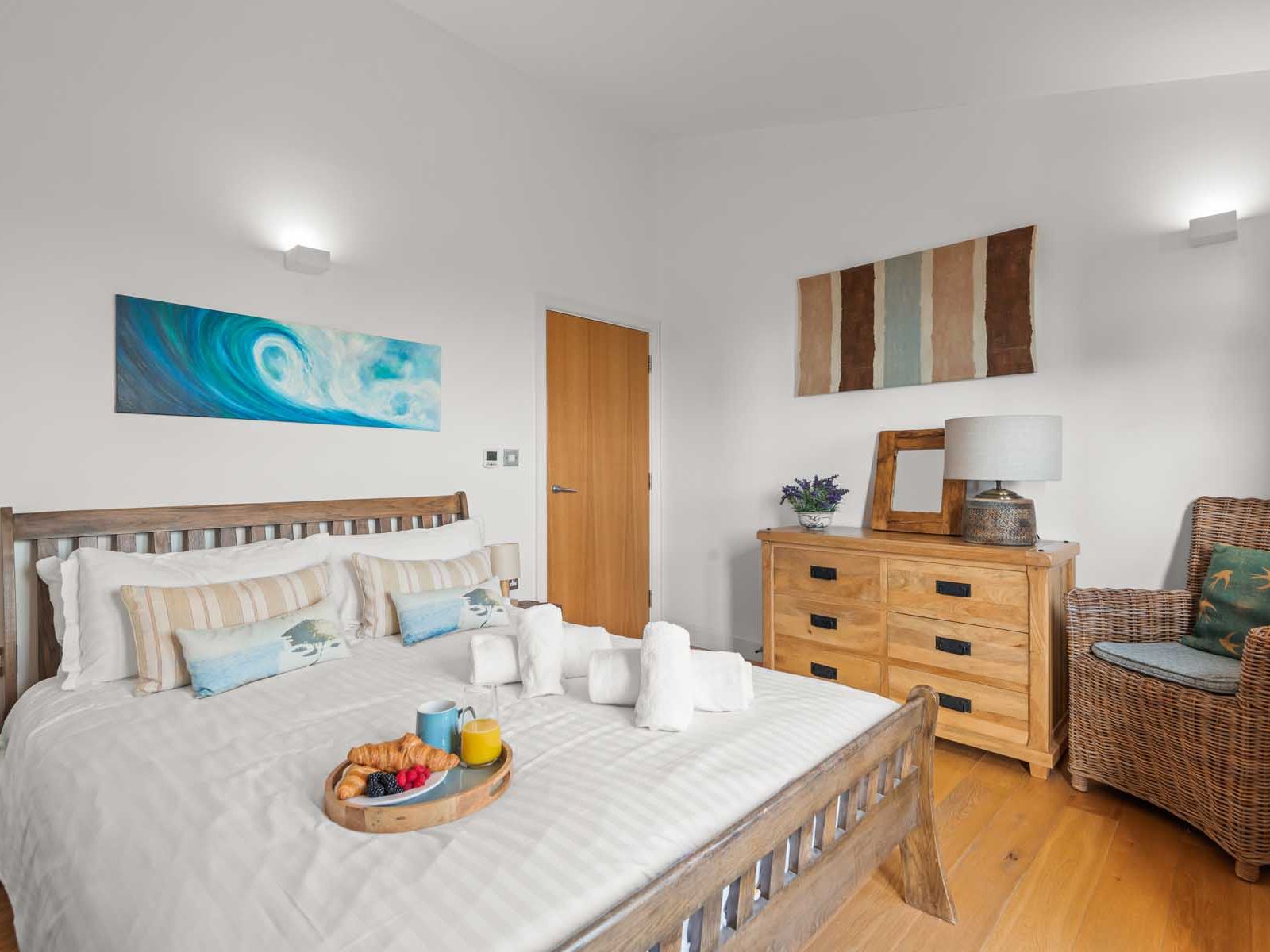 Cozy modern bedroom with a wooden bed, wicker chair, dresser, and breakfast tray on the bed