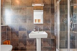 Modern bathroom with brown tiled walls, white sink, mirror, and glass shower enclosure