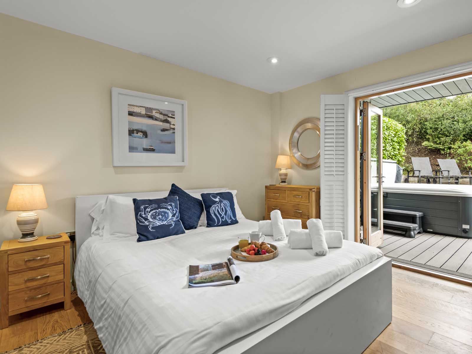 Cozy bedroom with white bed, wooden furniture, and open doors leading to a patio with hot tub and lounge chairs.