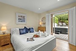 Cozy bedroom with white bed, wooden furniture, and open doors leading to a patio with hot tub and lounge chairs.