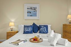 Cozy bedroom with white bedding, blue decorative pillows, and a breakfast tray with pastries, fruit, juice, and coffee on the bed.