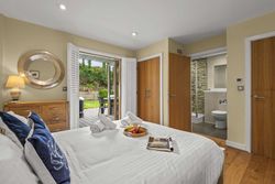 Modern bedroom with ensuite bathroom and doors opening to a patio with garden view.