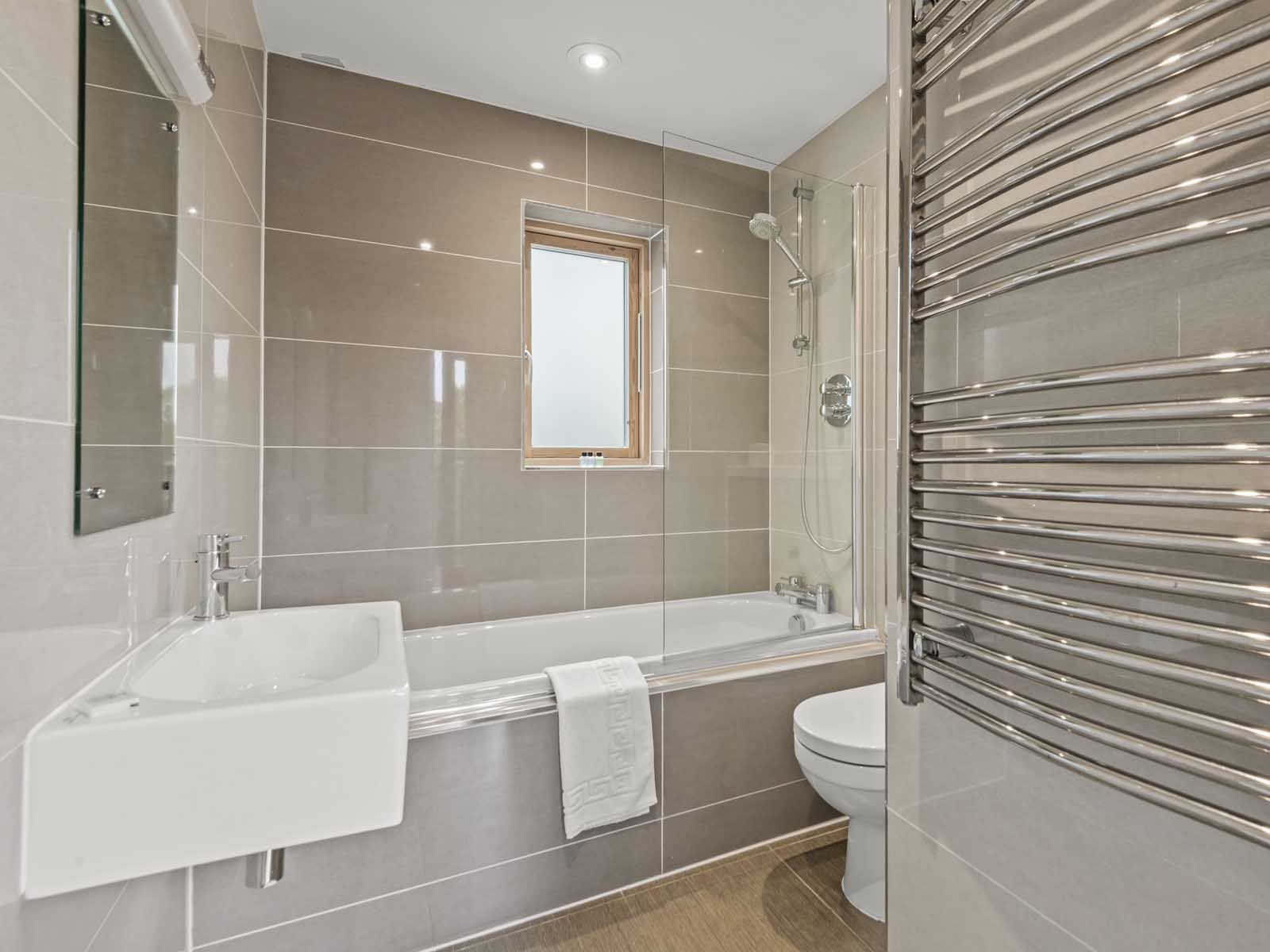 Modern bathroom with a bathtub, sink, toilet, and heated towel rail