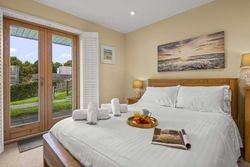 Cozy bedroom with a wooden bed, white linens, a tray with breakfast, rolled towels, and a view to a garden through glass doors.