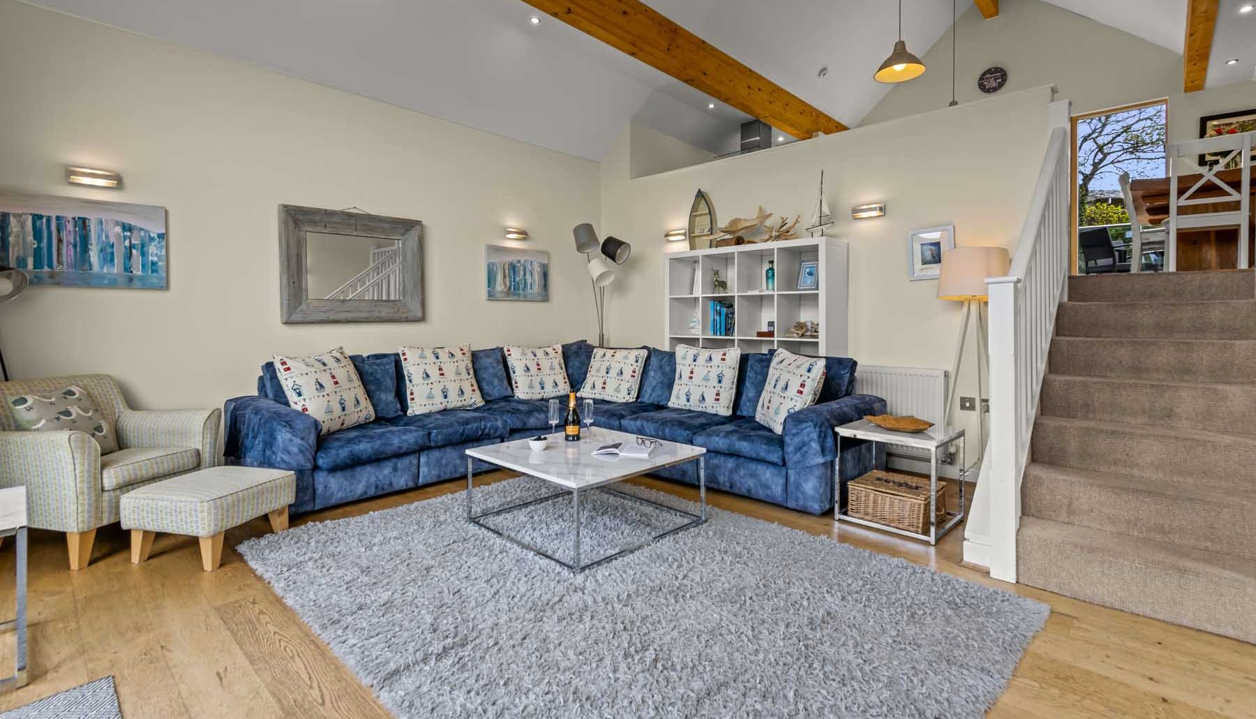 Modern living room with blue corner sofa, decorative pillows, and staircase leading to dining area