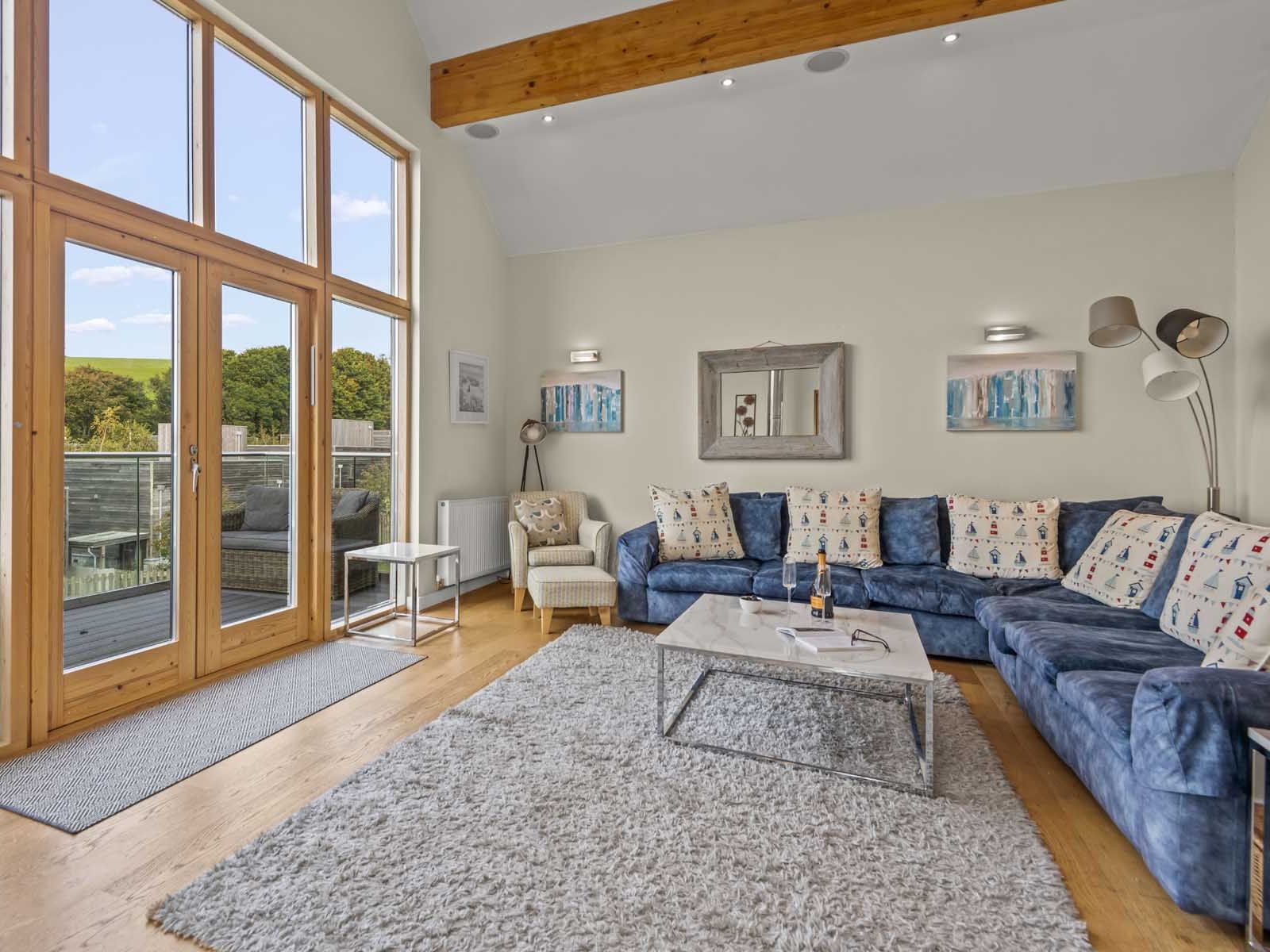 Modern living room with large windows, blue sectional sofa, and light wooden floors