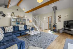 Modern living room with blue sectional sofa, wood stove, and exposed wooden ceiling beams.