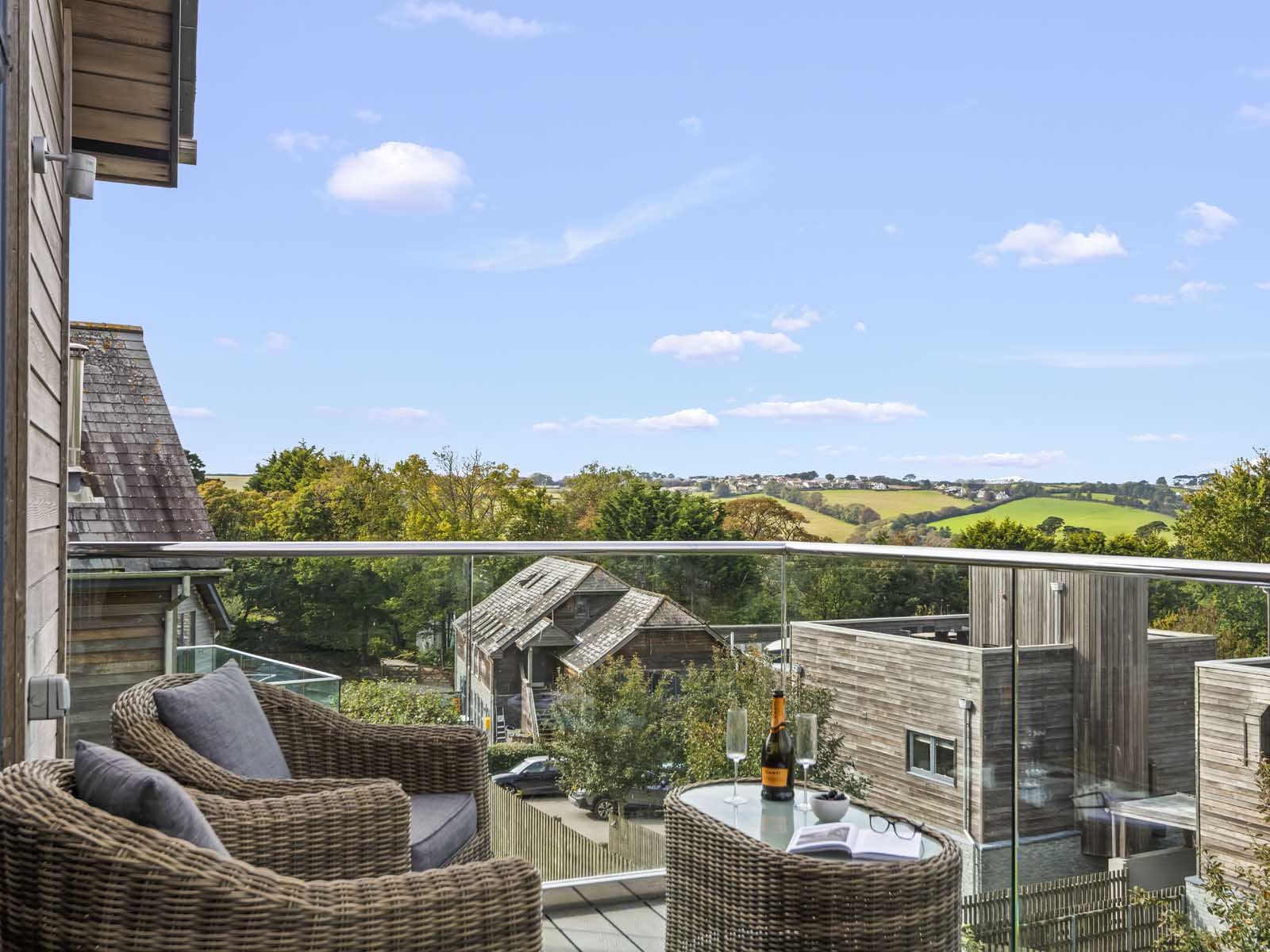 Balcony with wicker chairs and glass table overlooking countryside and modern wooden houses