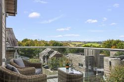 Balcony with wicker chairs and glass table overlooking countryside and modern wooden houses