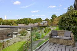 Balcony view with outdoor wicker sofa overlooking modern wooden houses and greenery