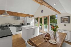 Modern kitchen and dining area with wooden beams, white cabinets, and large glass doors leading to an outdoor patio.