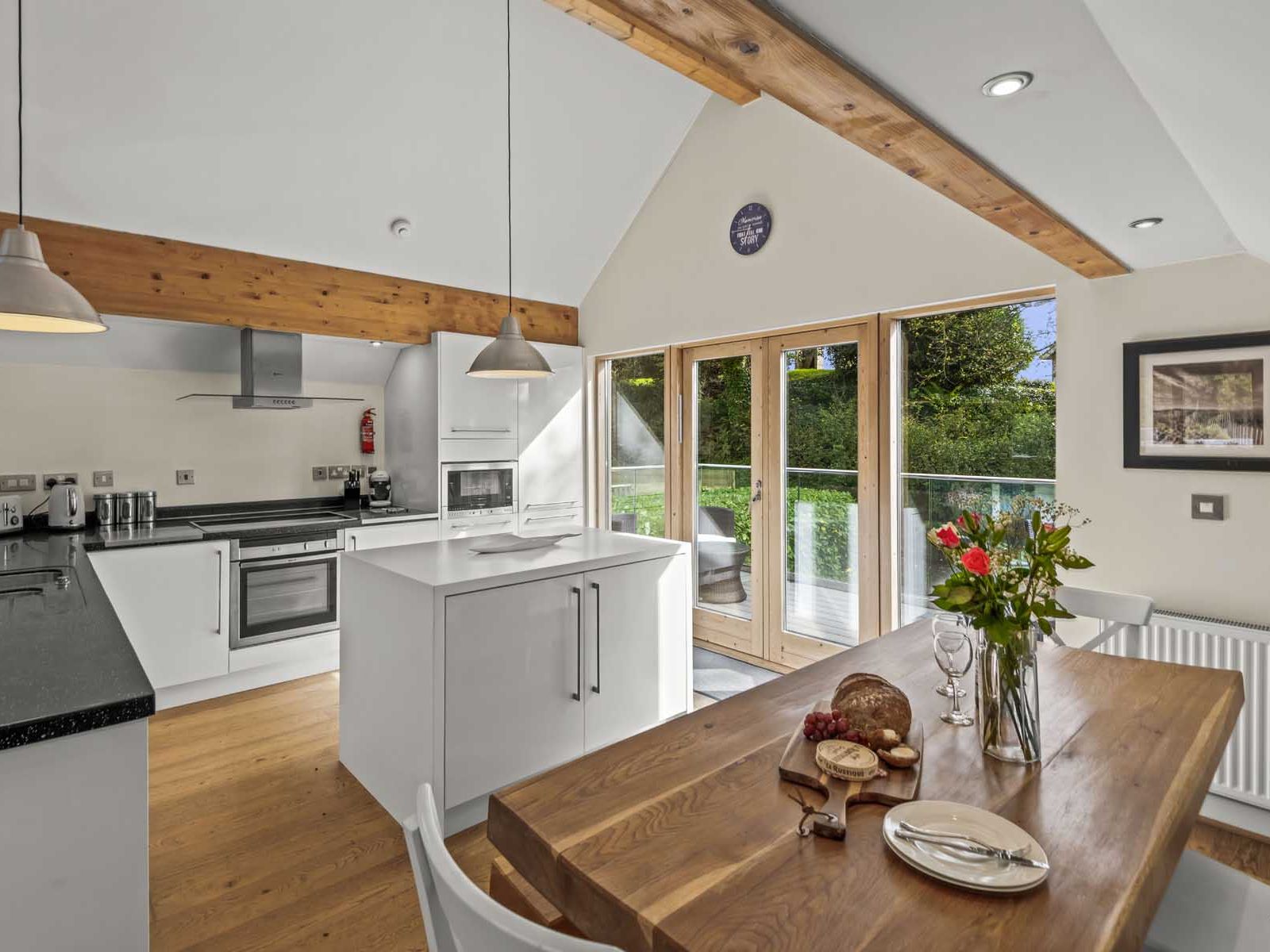 Modern kitchen and dining area with wooden beams, white cabinets, and large glass doors leading to an outdoor patio.