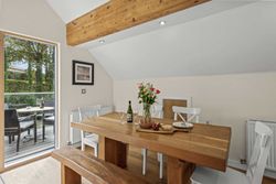 Modern dining area with wooden table, white chairs, and a view of an outdoor patio through a glass door.
