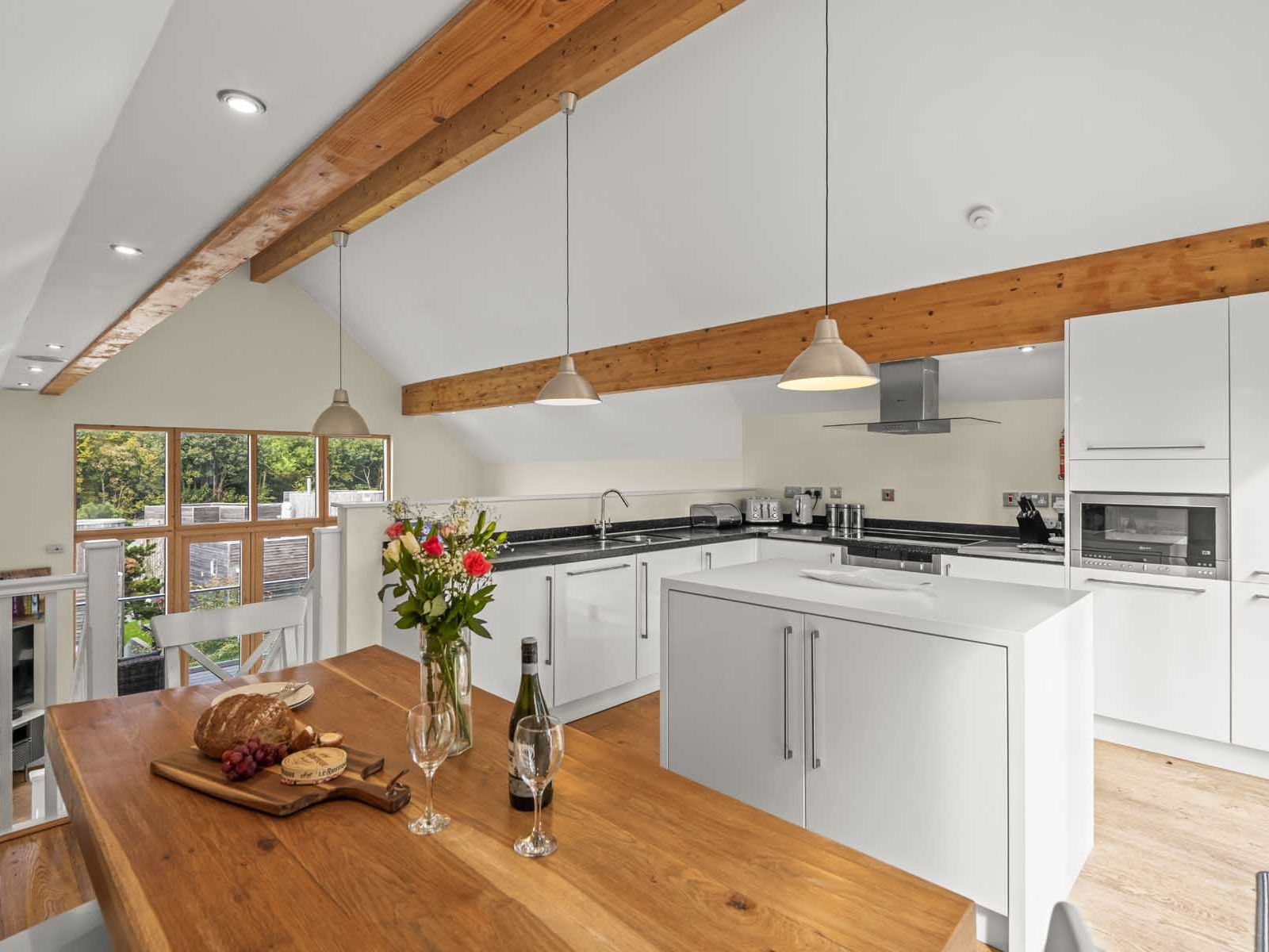 Modern open-plan kitchen with wooden beams, white cabinets, and a dining table set for two.