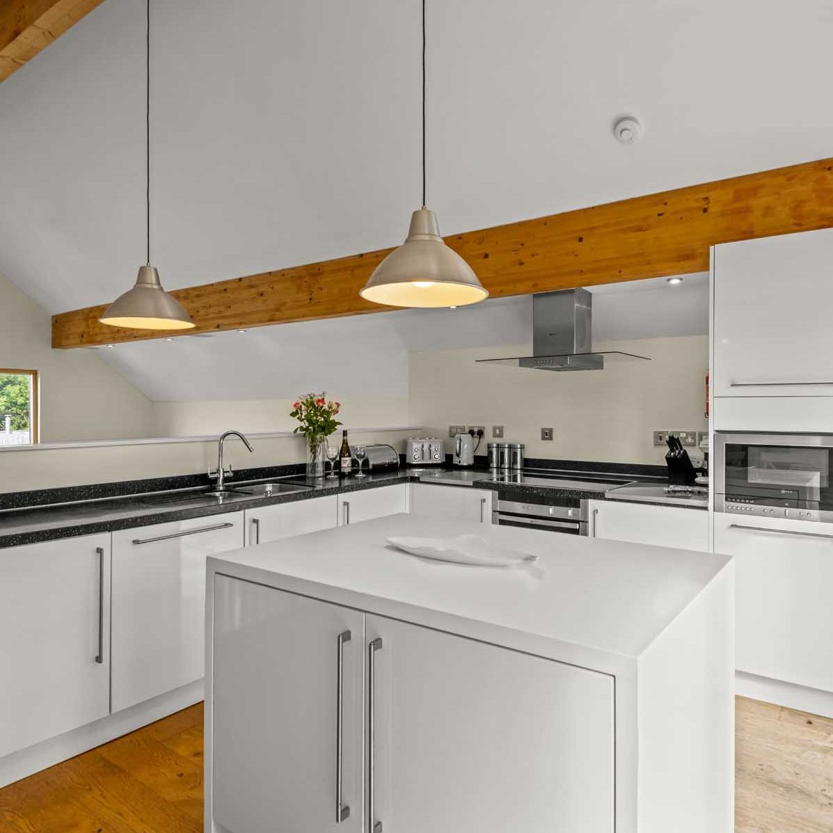 Modern kitchen with white cabinets, black countertops, and wooden beams.