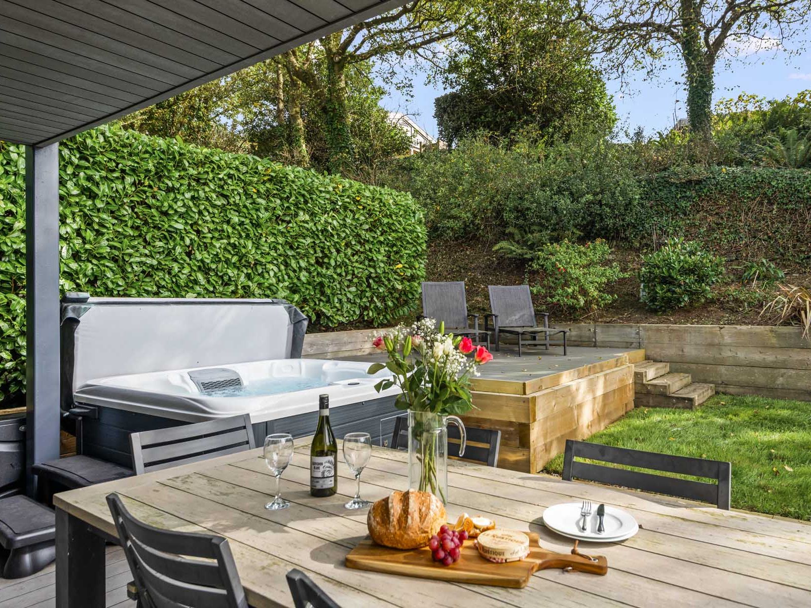 Outdoor patio with hot tub, dining table set for two, and garden loungers in a lush backyard.