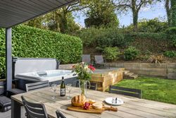 Outdoor patio with hot tub, dining table set for two, and garden loungers in a lush backyard.
