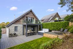 Modern house with stone and wood exterior, outdoor deck, hot tub, and balcony