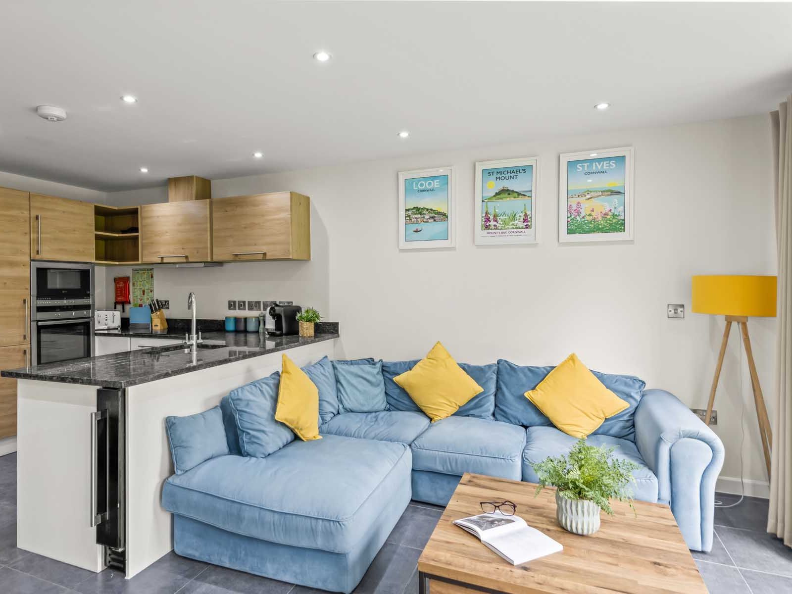 Modern open-plan kitchen and living area with blue sofa and yellow cushions