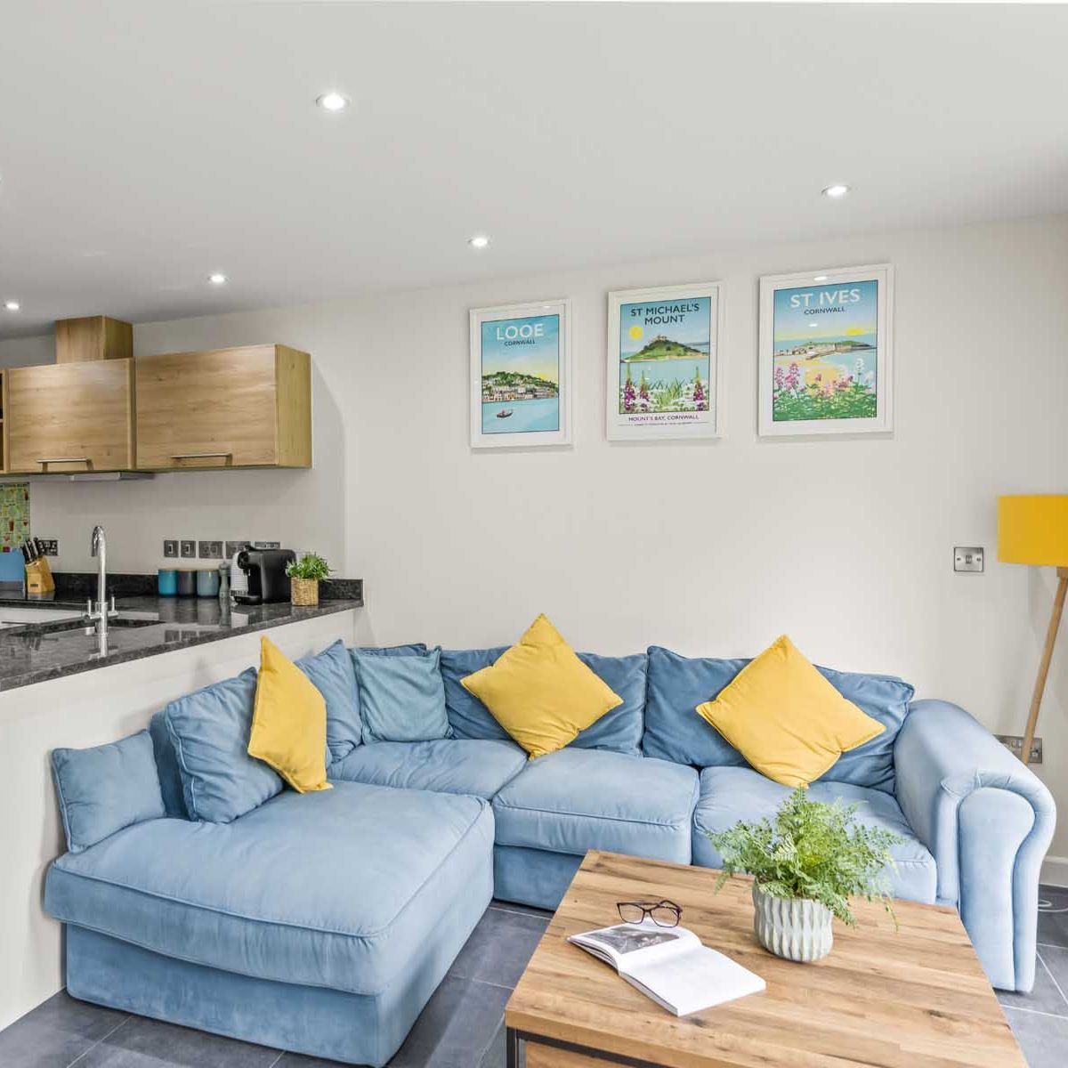 Modern open-plan kitchen and living area with blue sofa and yellow cushions