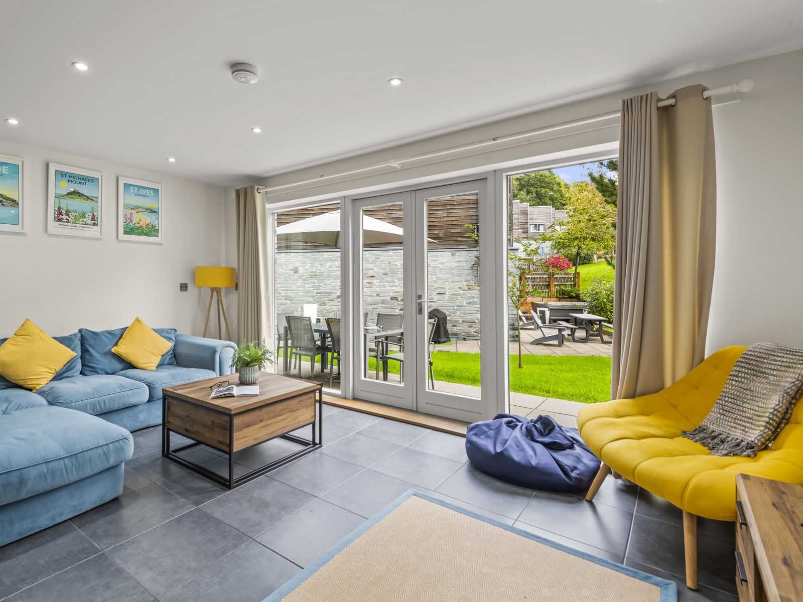 Modern living room with blue sofa, yellow chair, and large glass doors opening to a garden patio.