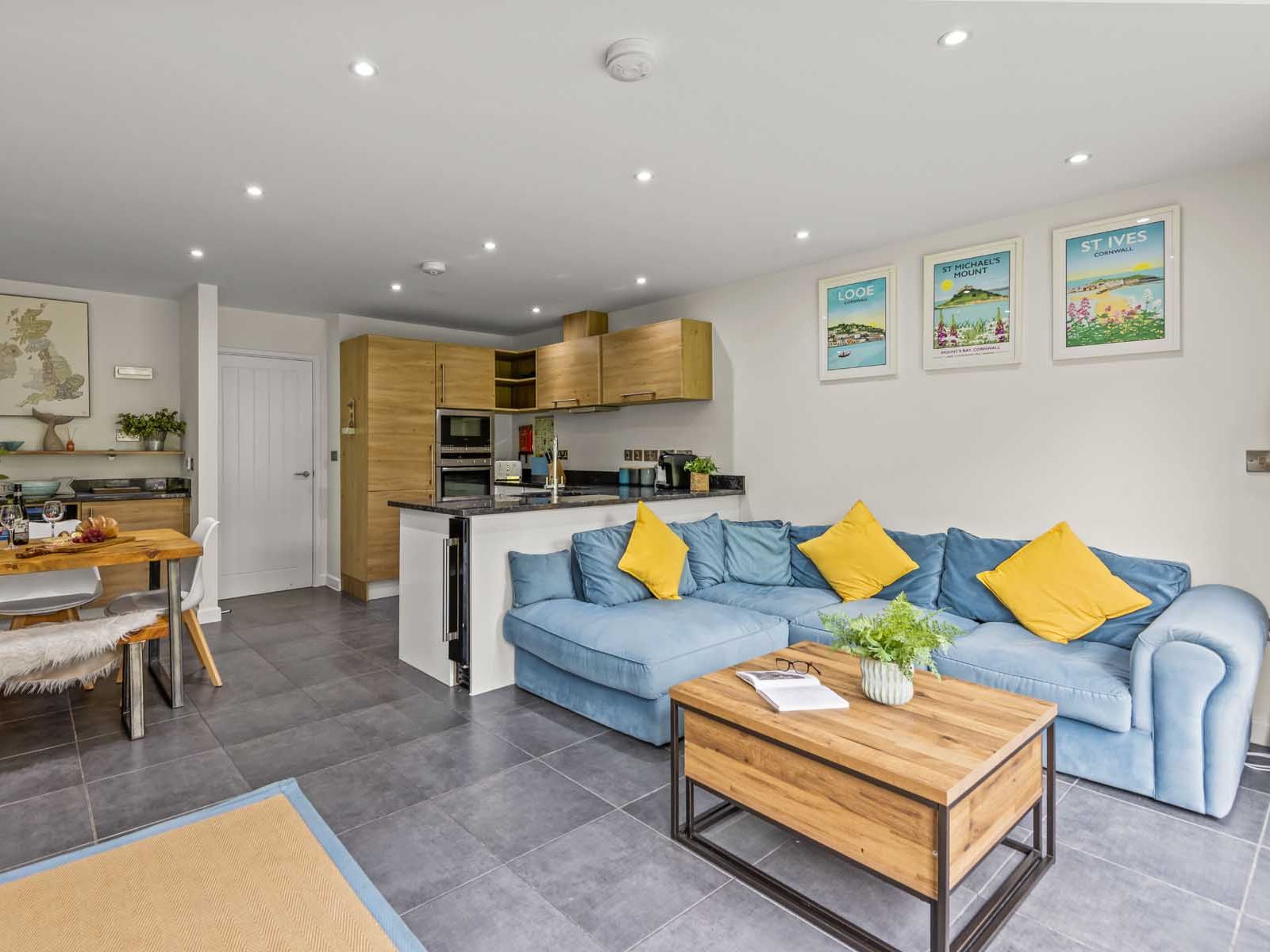 Modern open-plan kitchen and living room with blue sofa, wooden dining table, and decorative wall art.