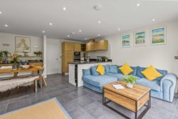 Modern open-plan kitchen and living room with blue sofa, wooden dining table, and decorative wall art.