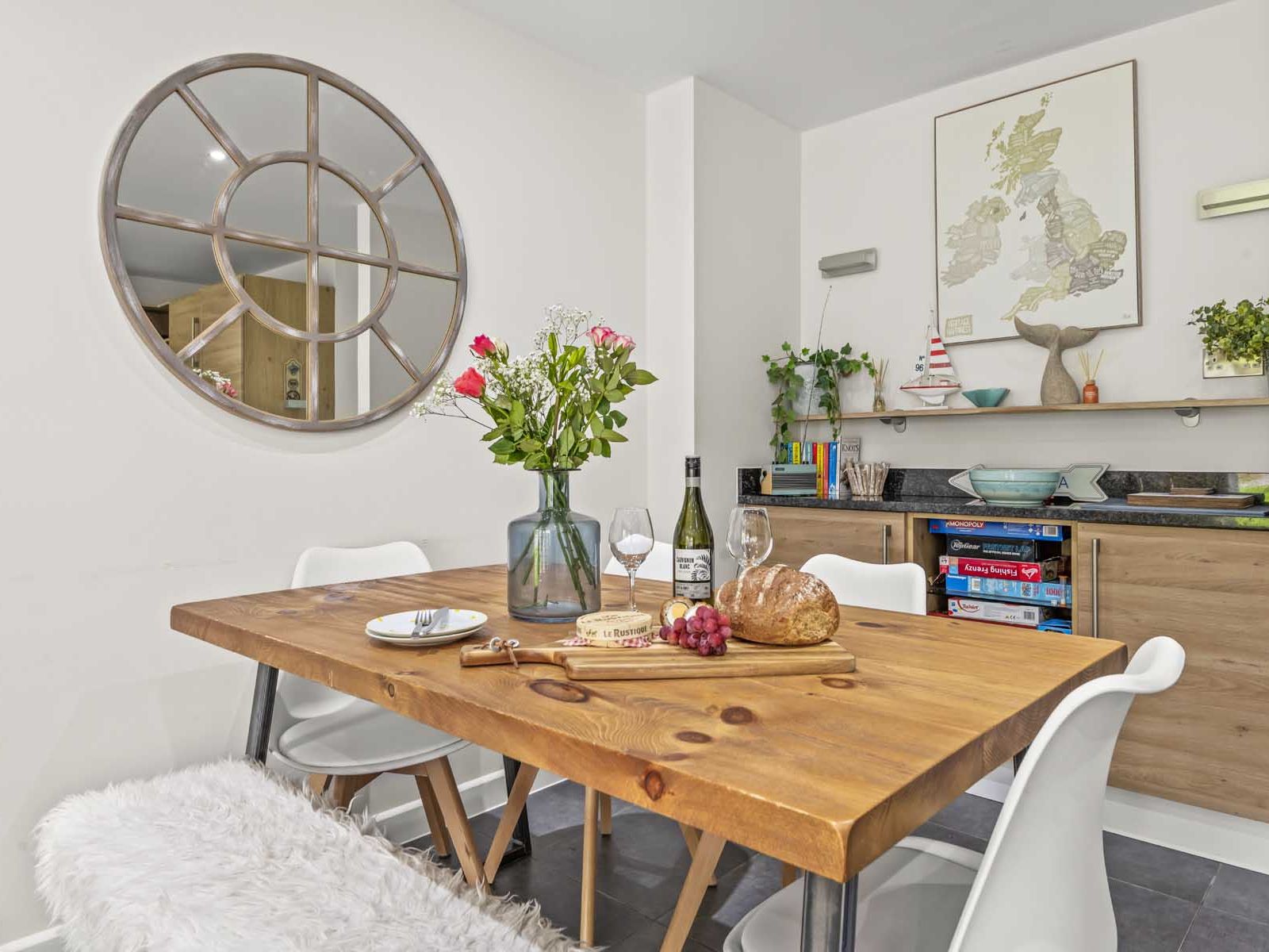 Modern dining room with wooden table, white chairs, a round mirror, and decorative shelves.